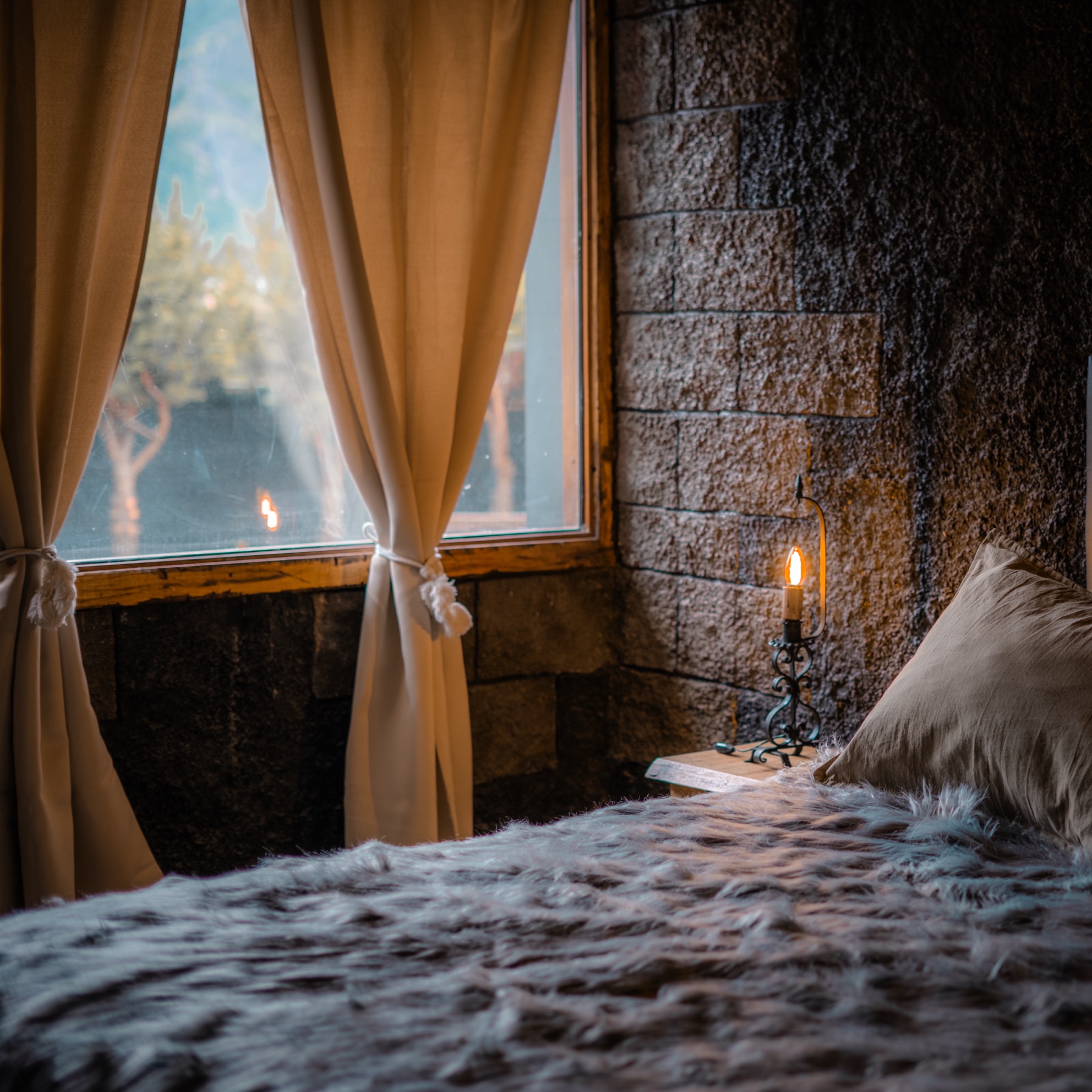 Alcoba con ventana, cortinas y vela junto a la pared de piedra
